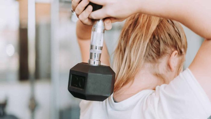 woman holding dumbbell in white crew-neck t-shirt