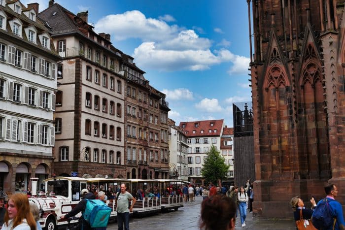 Visite de Strasbourg en petit train 1 a group of people walking down a street next to tall buildings