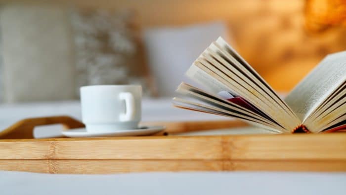 an open book on a bed with a cup of coffee