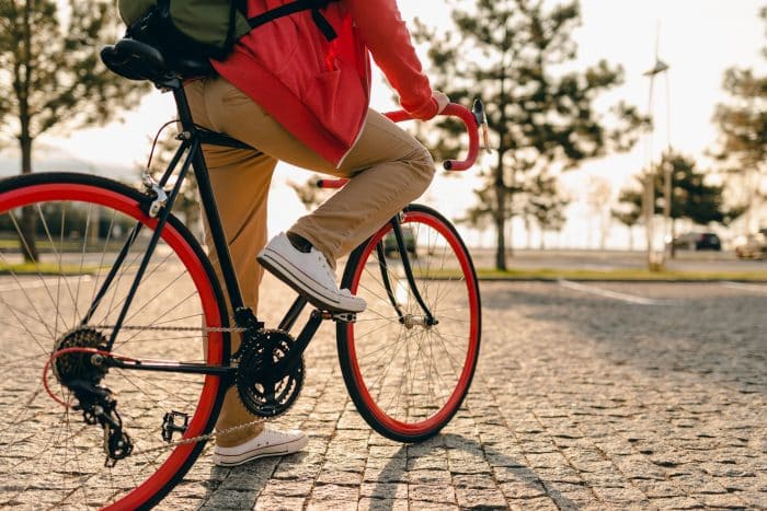 Cours d'initiation au vélo 1 close up legs sneakers hands steering wheel hipster style bearded man red hoodie beige trousers riding alone with backpack bicycle healthy active lifestyle traveler backpacker 1