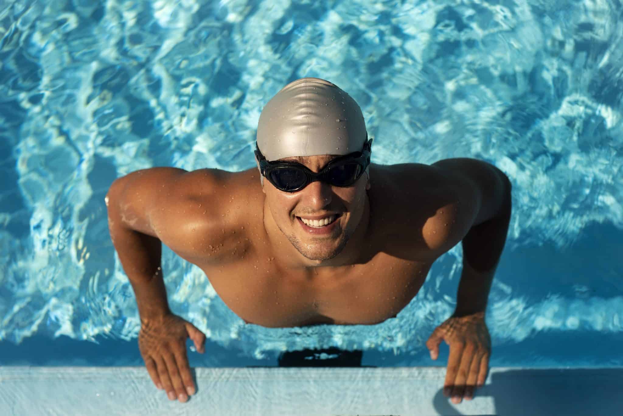 Cours d'initiation à la natation 3 smiley male swimmer posing with goggles cap pool 1 scaled